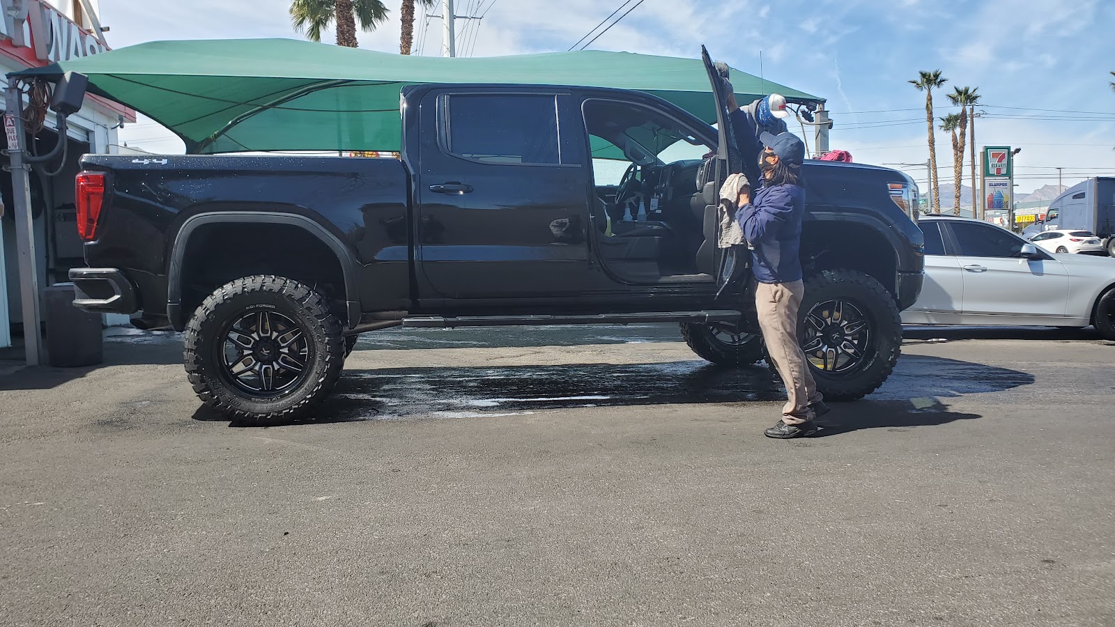 Detailer drying a large black lifted GMC truck under the canopy