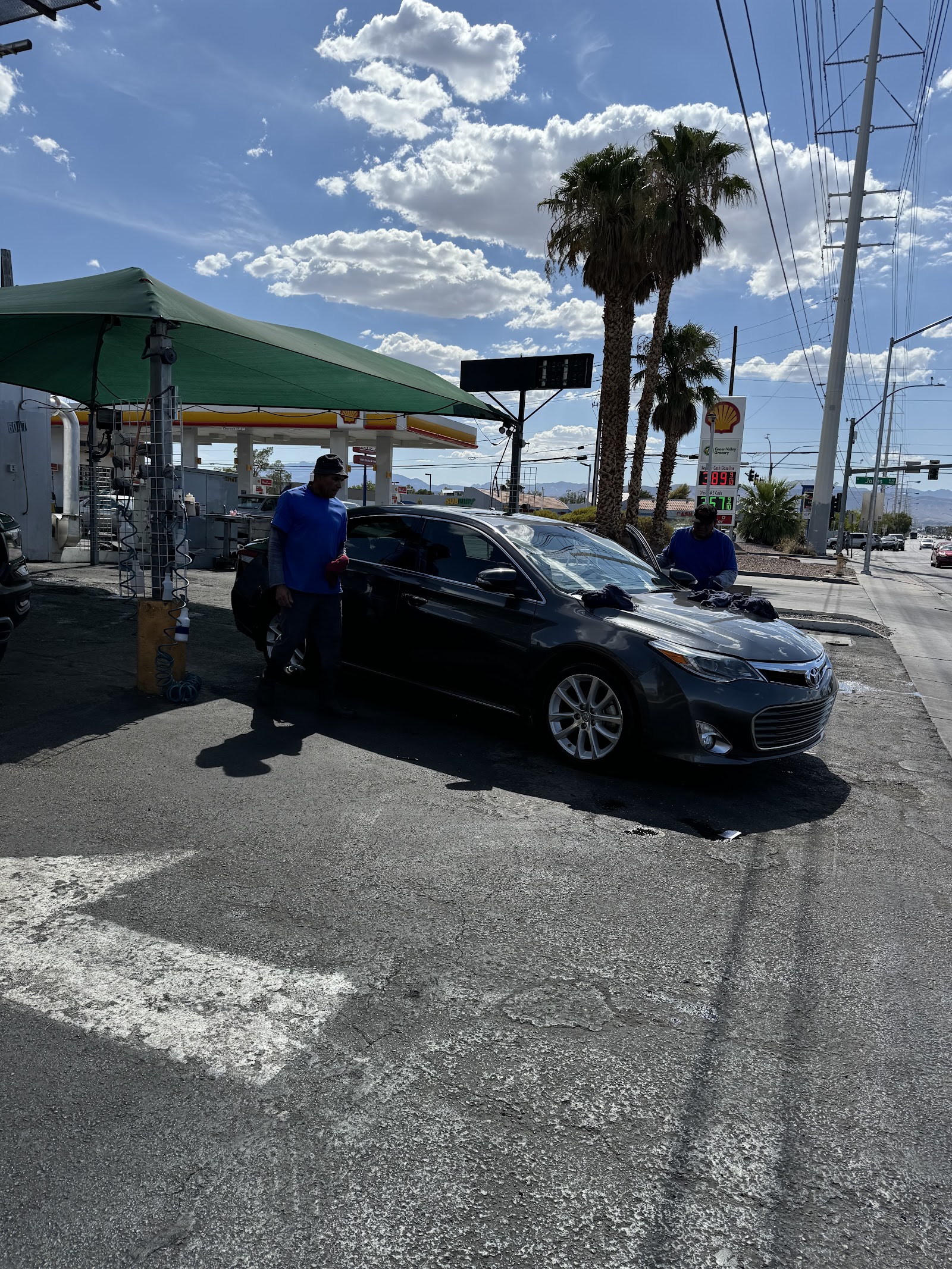 Workers hand washing a dark sedan at the outdoor car wash station